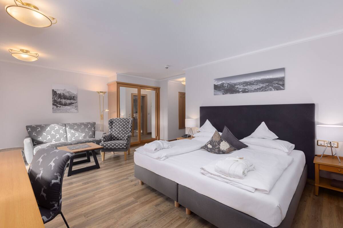 A hotel room with a bed, a sofa, a chair, a desk, and a mirror.