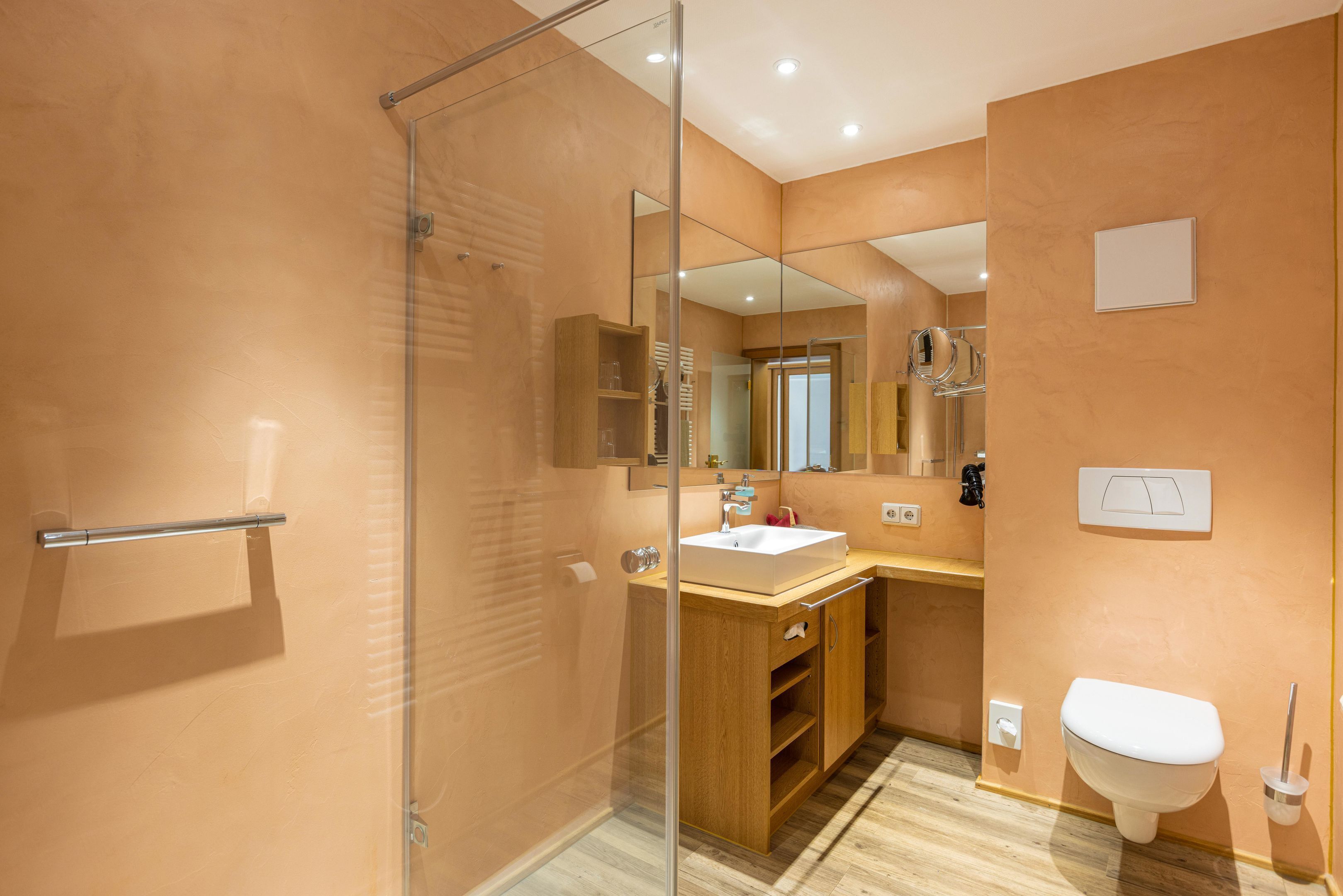 A modern bathroom with a glass shower enclosure, wooden vanity, and a white toilet.