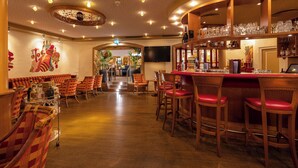 A bar area with wooden bar stools, a counter with glasses and bottles, and a seating area with patterned sofas and chairs. - IFA Alpenhof Wildental Hotel Kleinwalsertal (Mittelberg)