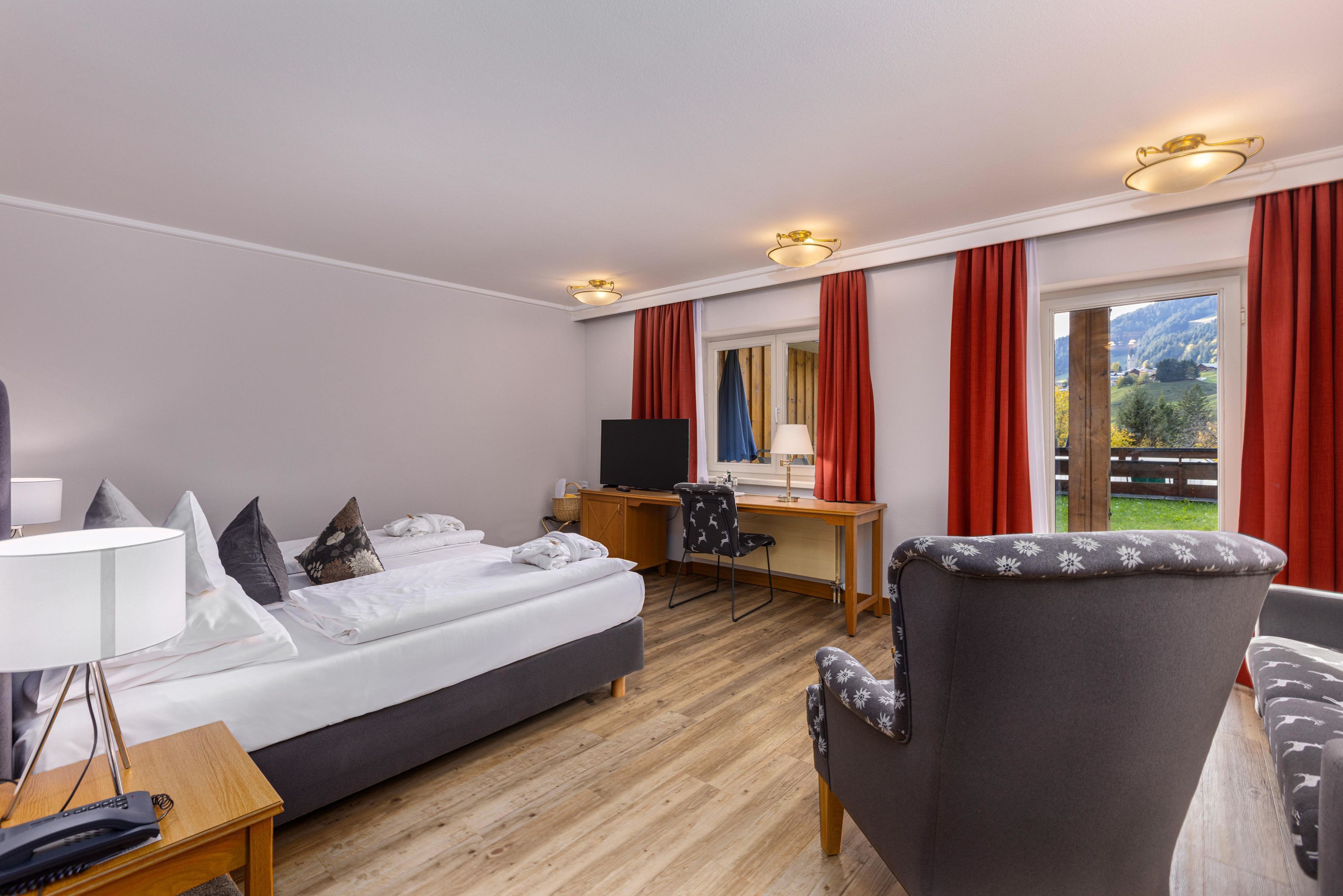 A hotel room with a bed, desk, chair, TV, and a view of the outdoors.
