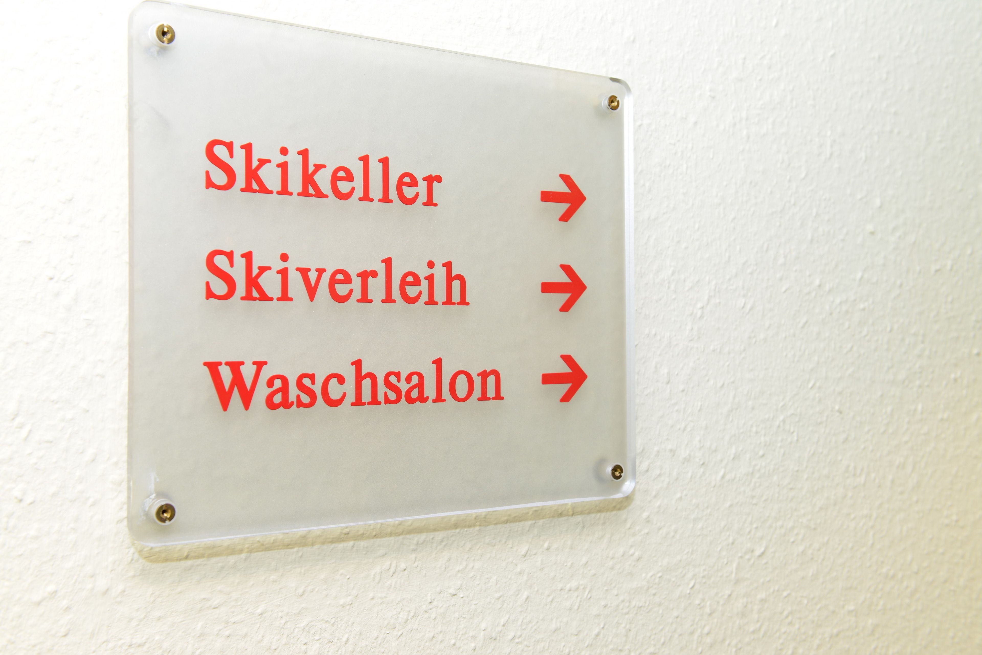 A directional sign with arrows pointing to 'Skikeller,' 'Skiverleih,' and 'Waschsalon.'