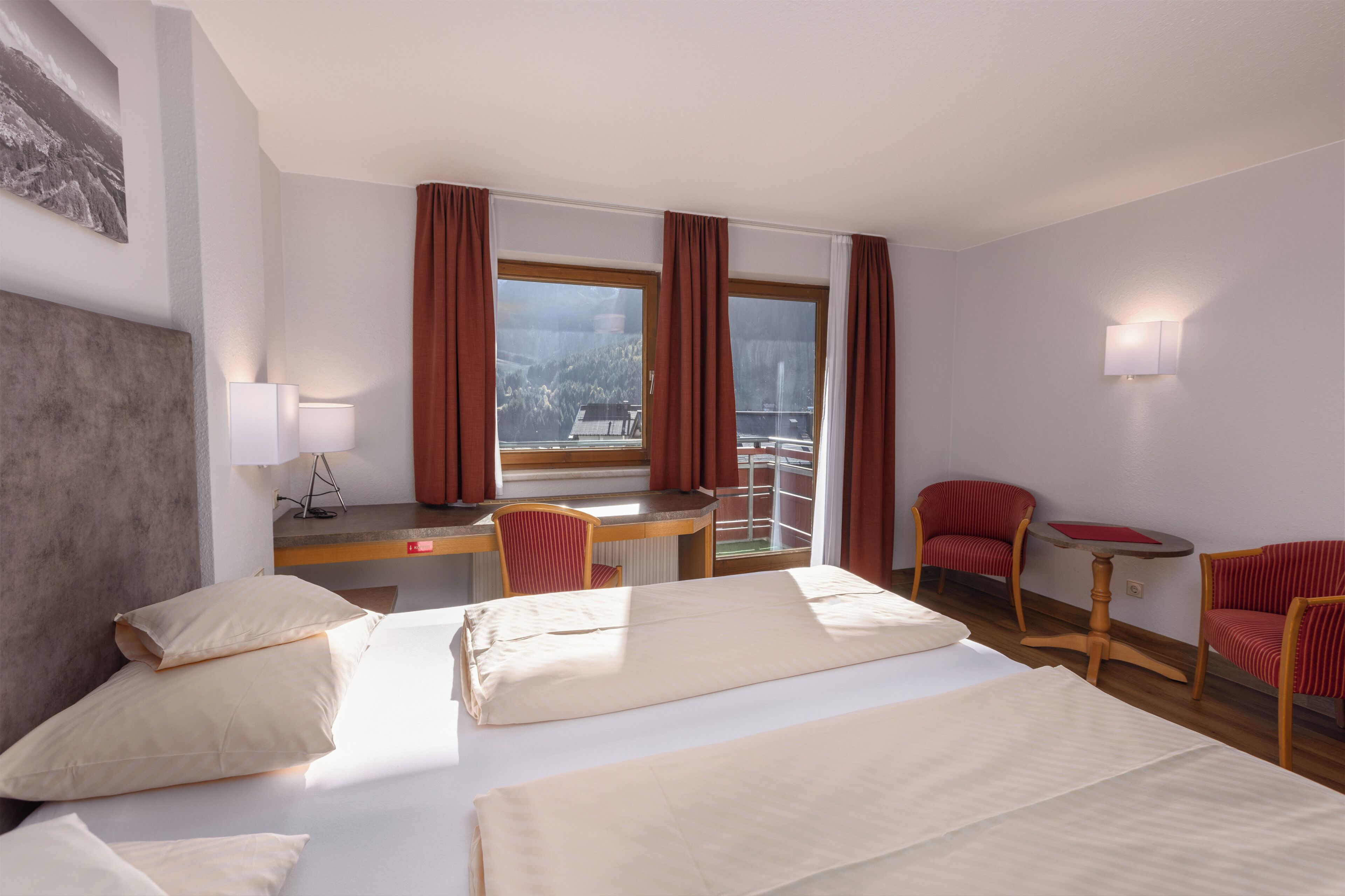 Una habitación de hotel con una cama, dos sillas, un escritorio, una lámpara y una ventana con cortinas.