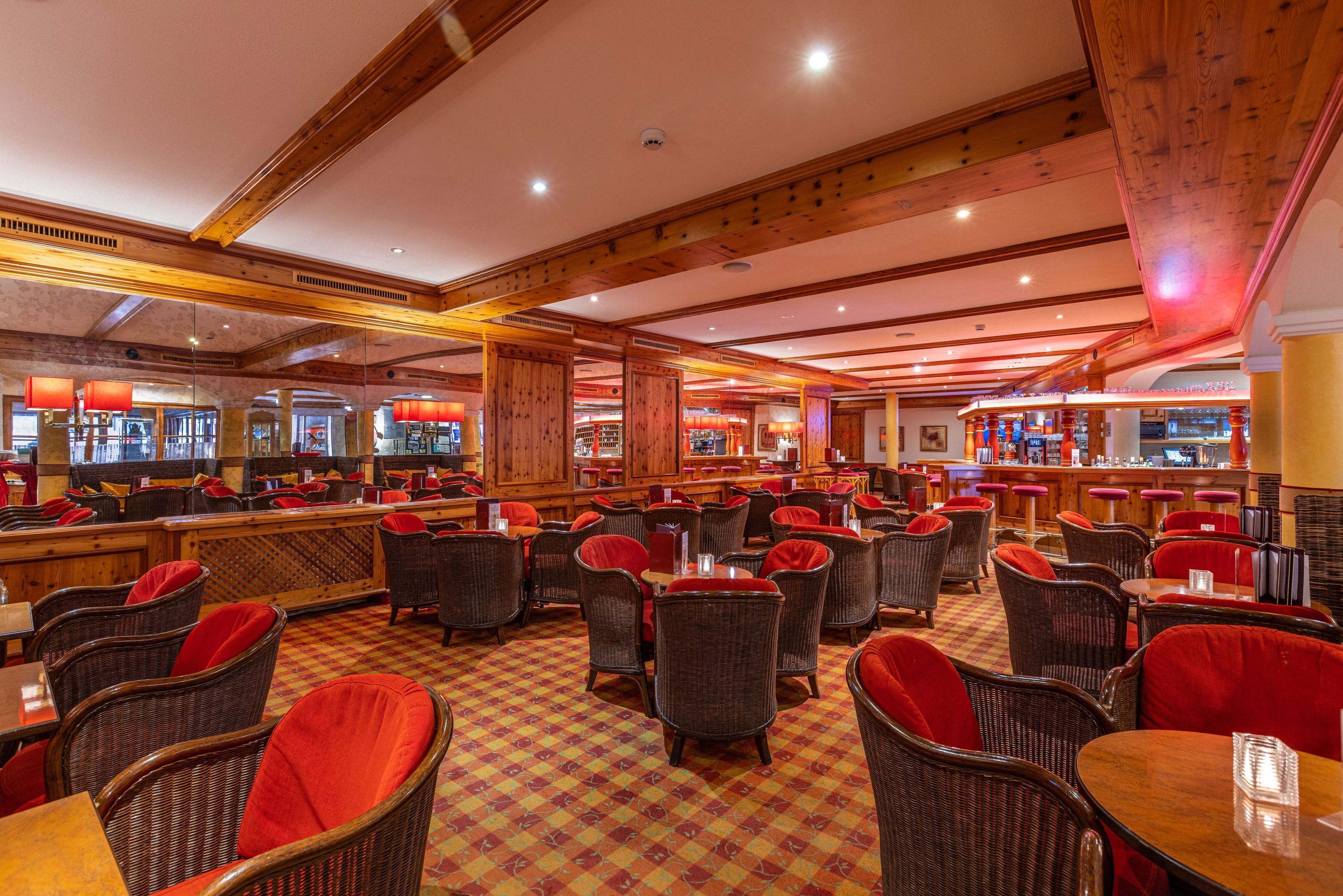 Un restaurant avec des chaises en osier et des coussins rouges, des poutres en bois au plafond et un sol à carreaux.