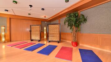 A spacious room with wooden flooring, exercise mats, a large potted plant, and a wall-mounted screen.