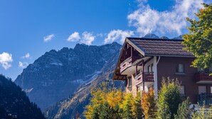 Un chalet de montagne doté d’un balcon, entouré d’arbres et de montagnes.
