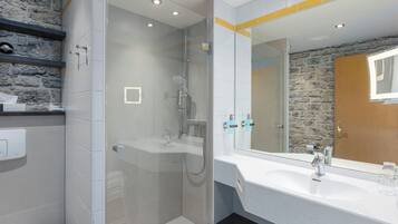 Un baño moderno con ducha envuelta en vidrio, un lavabo blanco y un espejo grande.