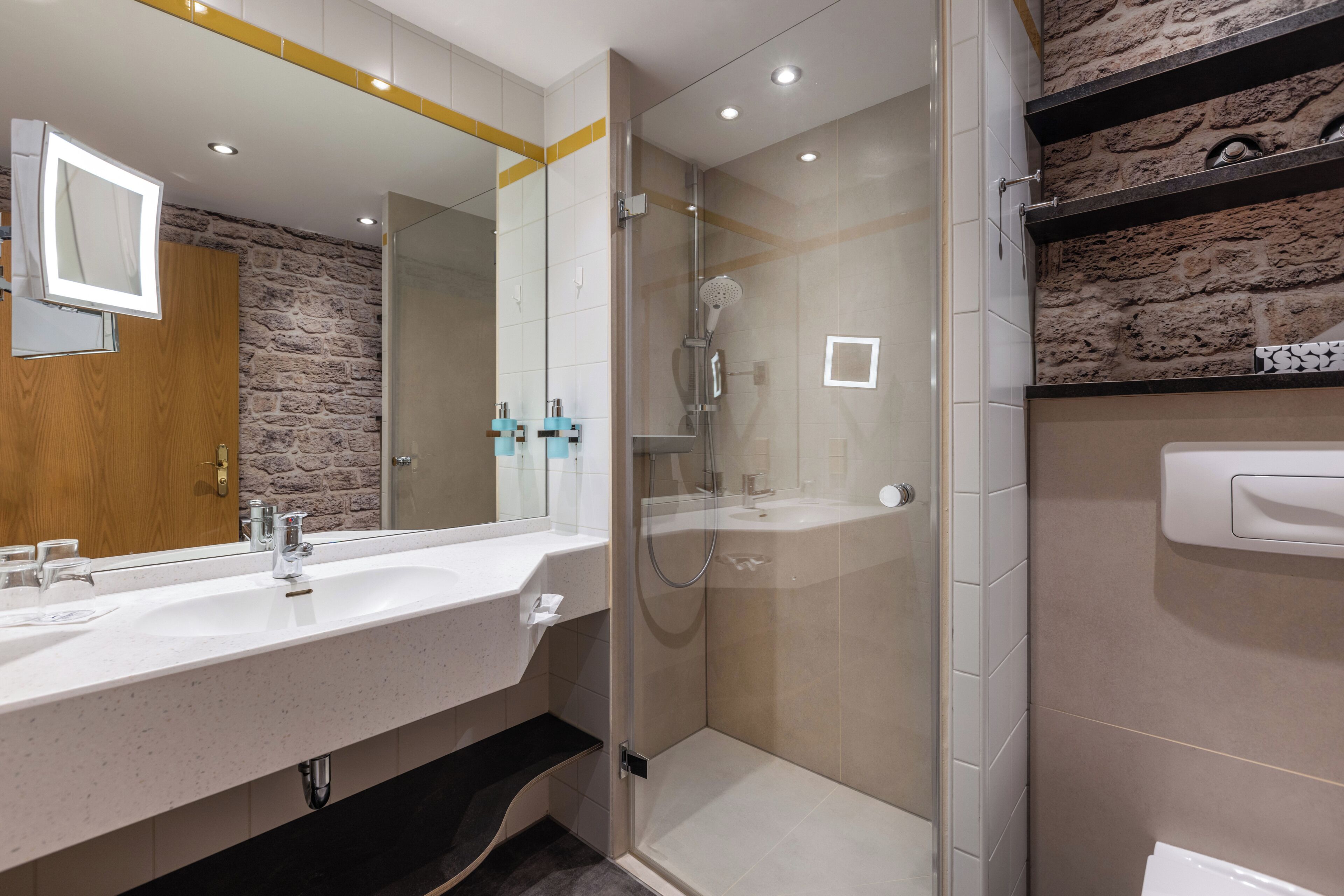 Un baño moderno con un espejo grande, dos lavamanos, una ducha y una pared de piedra.