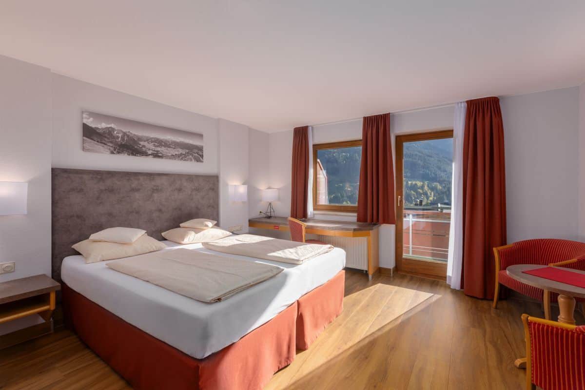A hotel room with a bed, desk, chair, and a view of mountains.