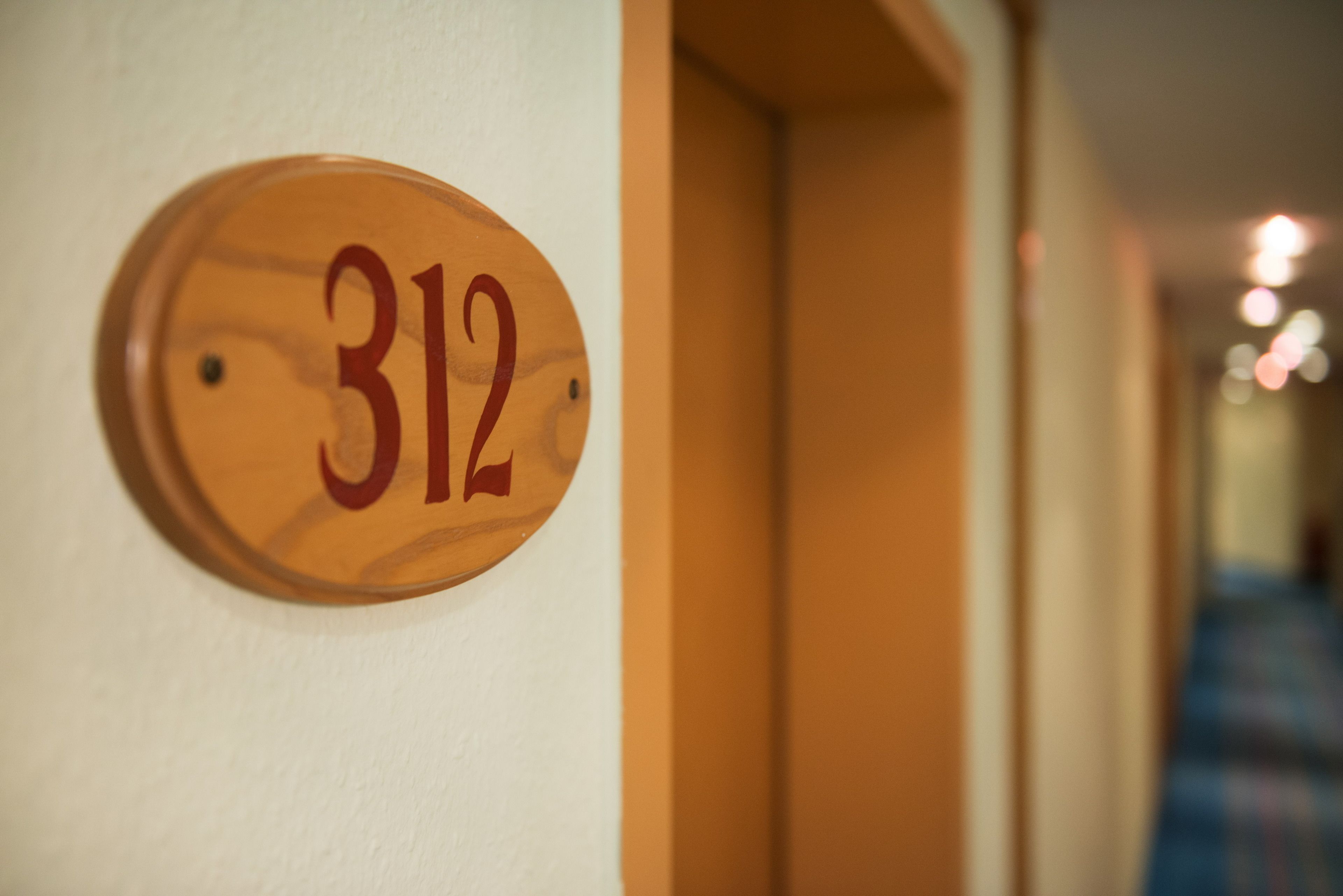 A wooden number plate with the number 312 on a white wall.
