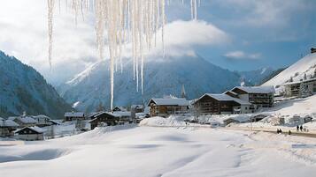 Un village de montagne enneigé, avec des bâtiments en bois et une église, entouré de collines recouvertes de neige.