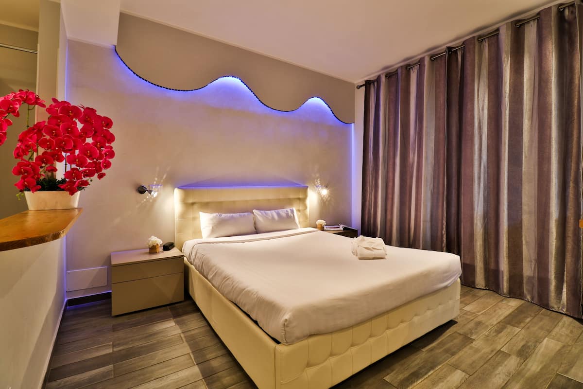 A modern hotel room with a large bed, a bedside table, a nightstand, and a wall-mounted light fixture.