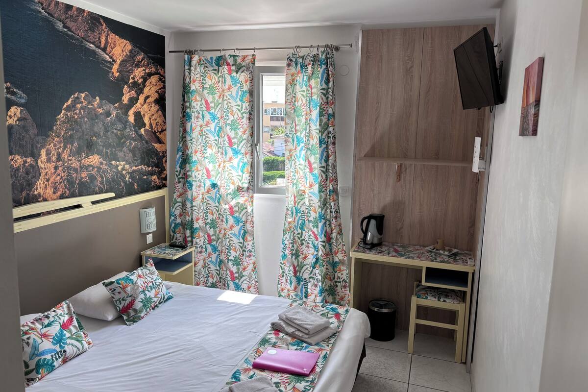 A hotel room with a bed, a desk, a TV, and a window with curtains.