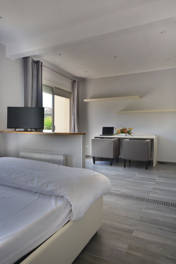 A modern hotel room with a large bed, a desk with a laptop, and a TV on a shelf. - Hôtel de la Mer (Vallauris)