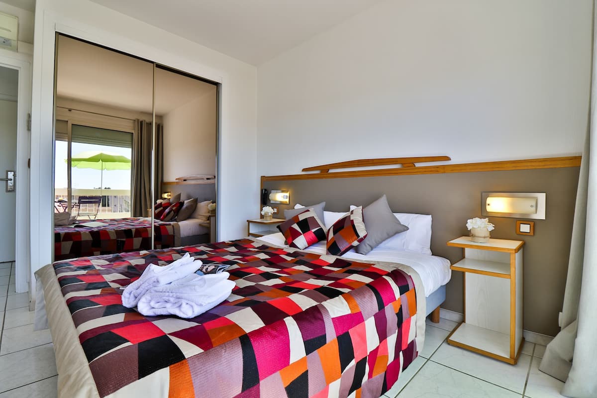 A hotel room with a large bed, a bedside table, a nightstand, and a view of the outside.