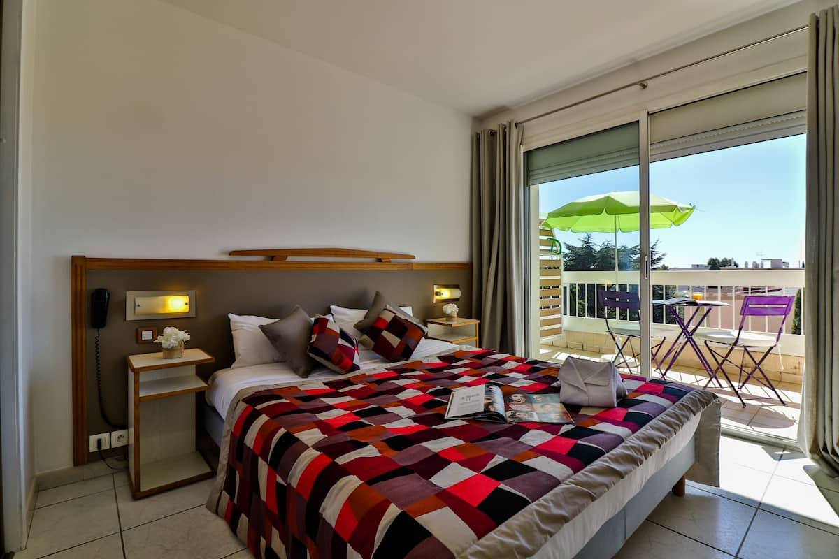 A hotel room with a bed, nightstands, a green umbrella, and a balcony with chairs.