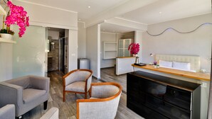 A modern living room with a sofa, chairs, a kitchen area with a dining table, and a bedroom with a bed and nightstand. - Hôtel de la Mer (Vallauris)