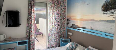 A hotel room with a bed, a desk, a chair, a TV, and a scenic mural.