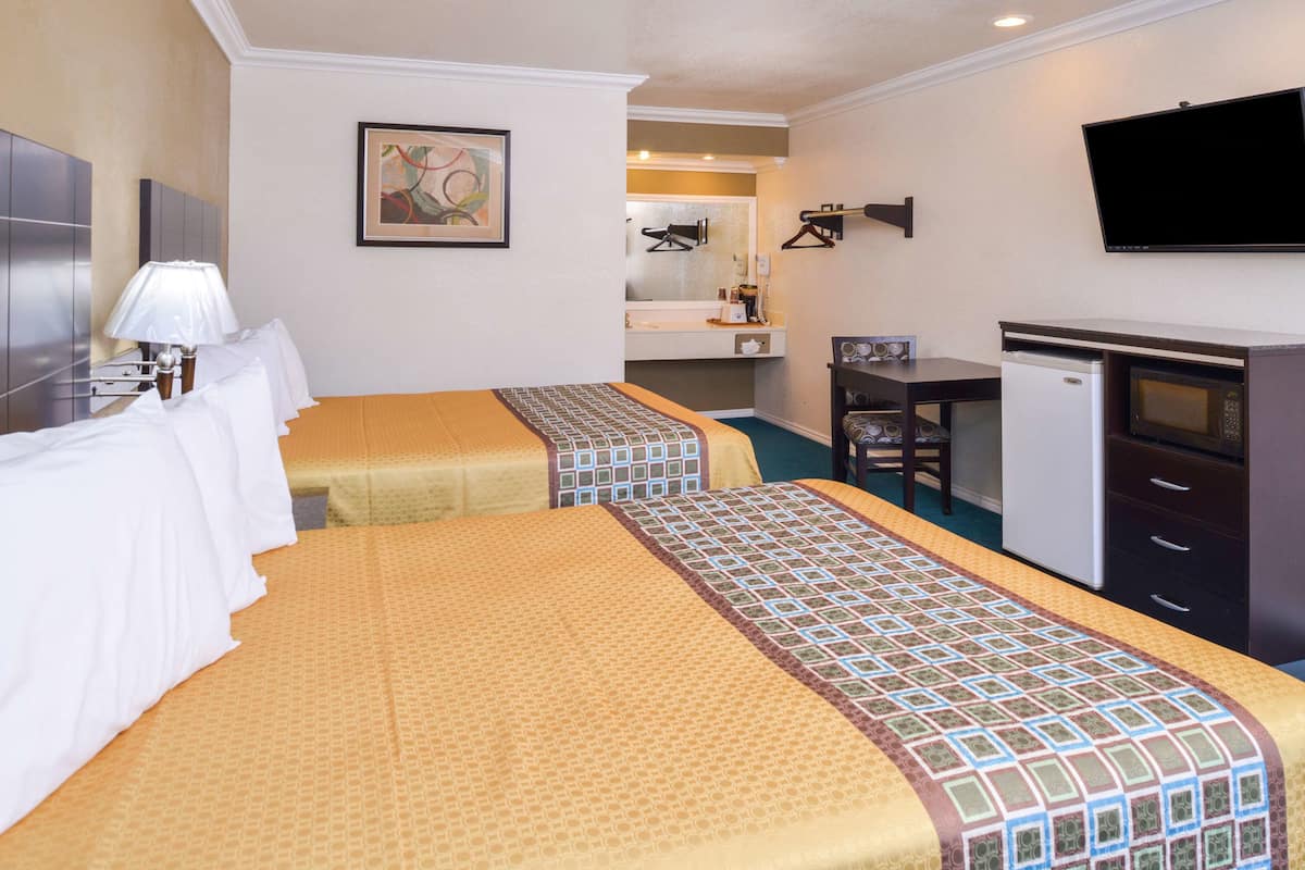 Une chambre d’hôtel avec deux lits, un bureau, un réfrigérateur, une télévision et une salle de bain que l’on aperçoit à l’arrière-plan.