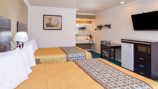 A hotel room with two beds, a desk, a refrigerator, a television, and a bathroom visible in the background.