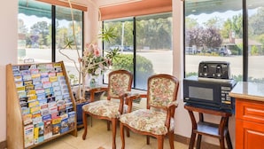 A room with a wooden chair, a small table, a microwave, and a bulletin board with travel brochures.
