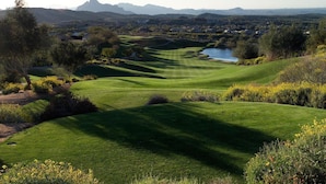 A golf course with a lake, surrounded by trees and hills.