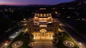 A large, historic building with a central dome and symmetrical wings, surrounded by well-maintained lawns and a paved plaza.