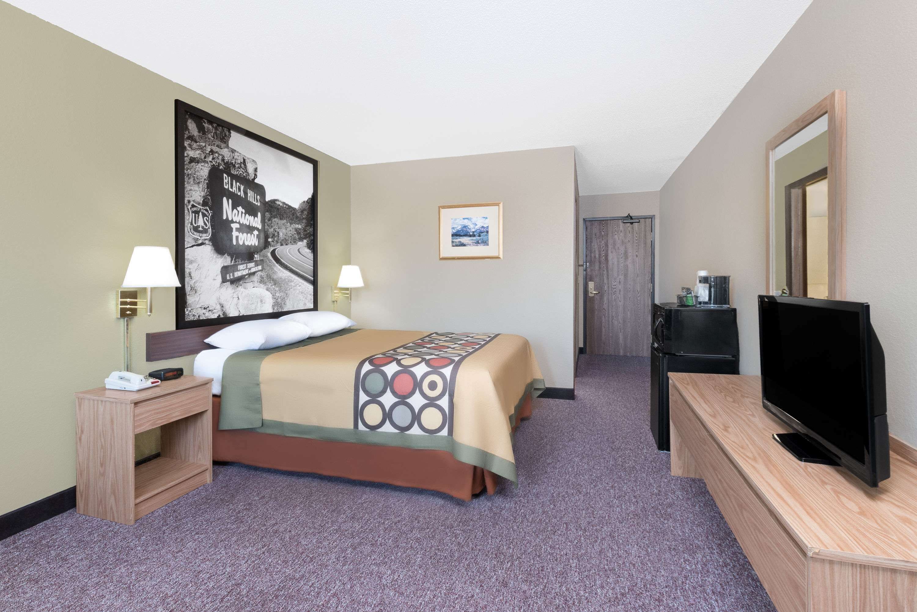 A hotel room with a bed, two bedside tables with lamps, a television on a wooden stand, and a framed picture on the wall.