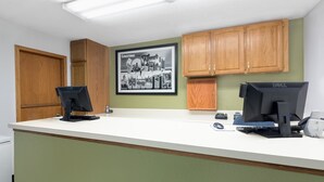 Un mostrador de recepción con dos monitores, armarios de madera y un cuadro en la pared.