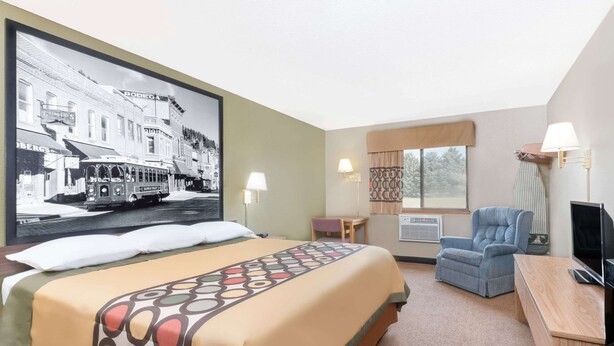 A hotel room with a large bed, a desk, a chair, and a television. - Super 8 by Wyndham Winner SD (Winner)