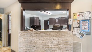 A reception area with a stone counter, a computer, and a bulletin board with various notices. - Colstrip Inn & Suites (Colstrip)