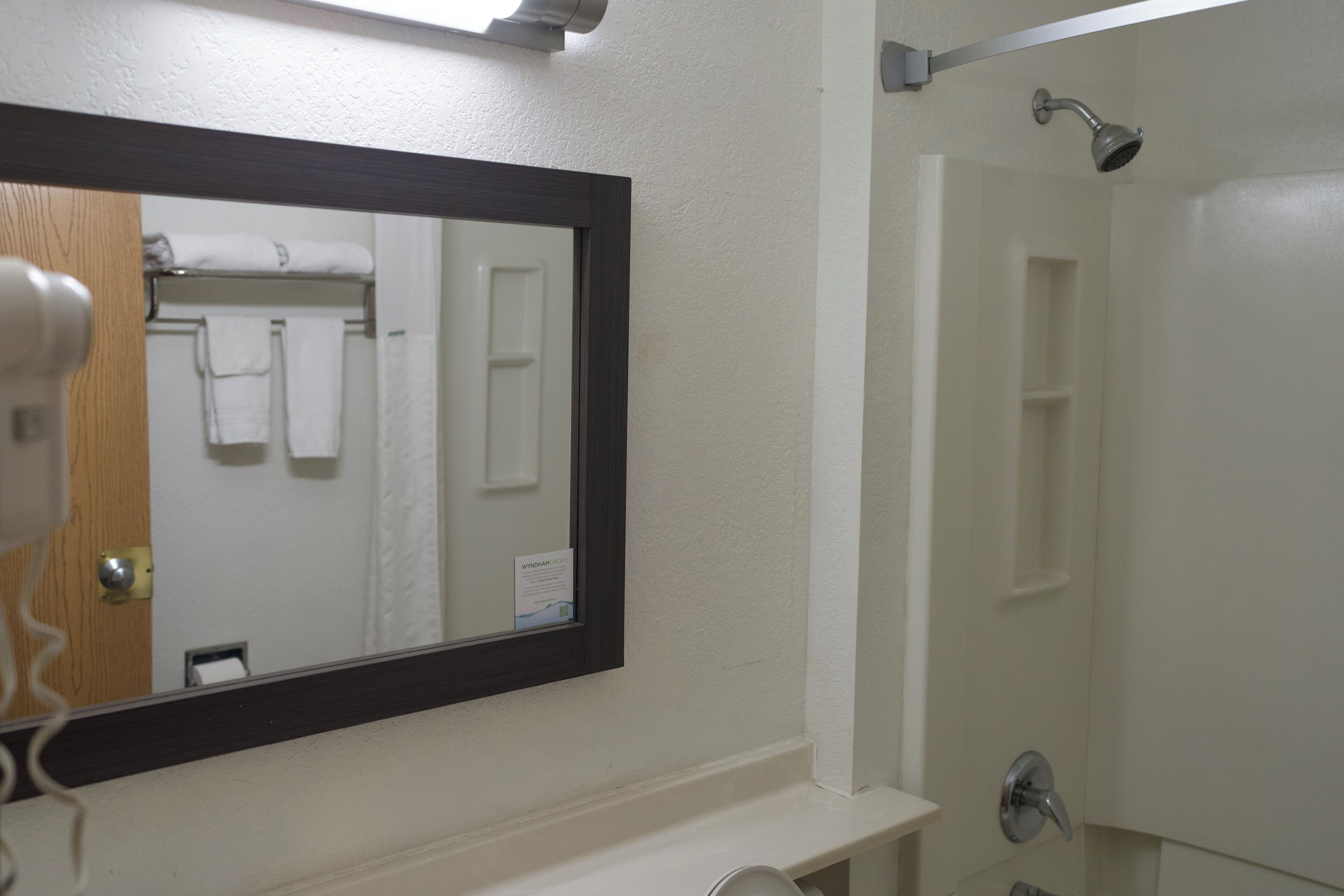 A bathroom with a large mirror, a shower, and a towel rack with towels.