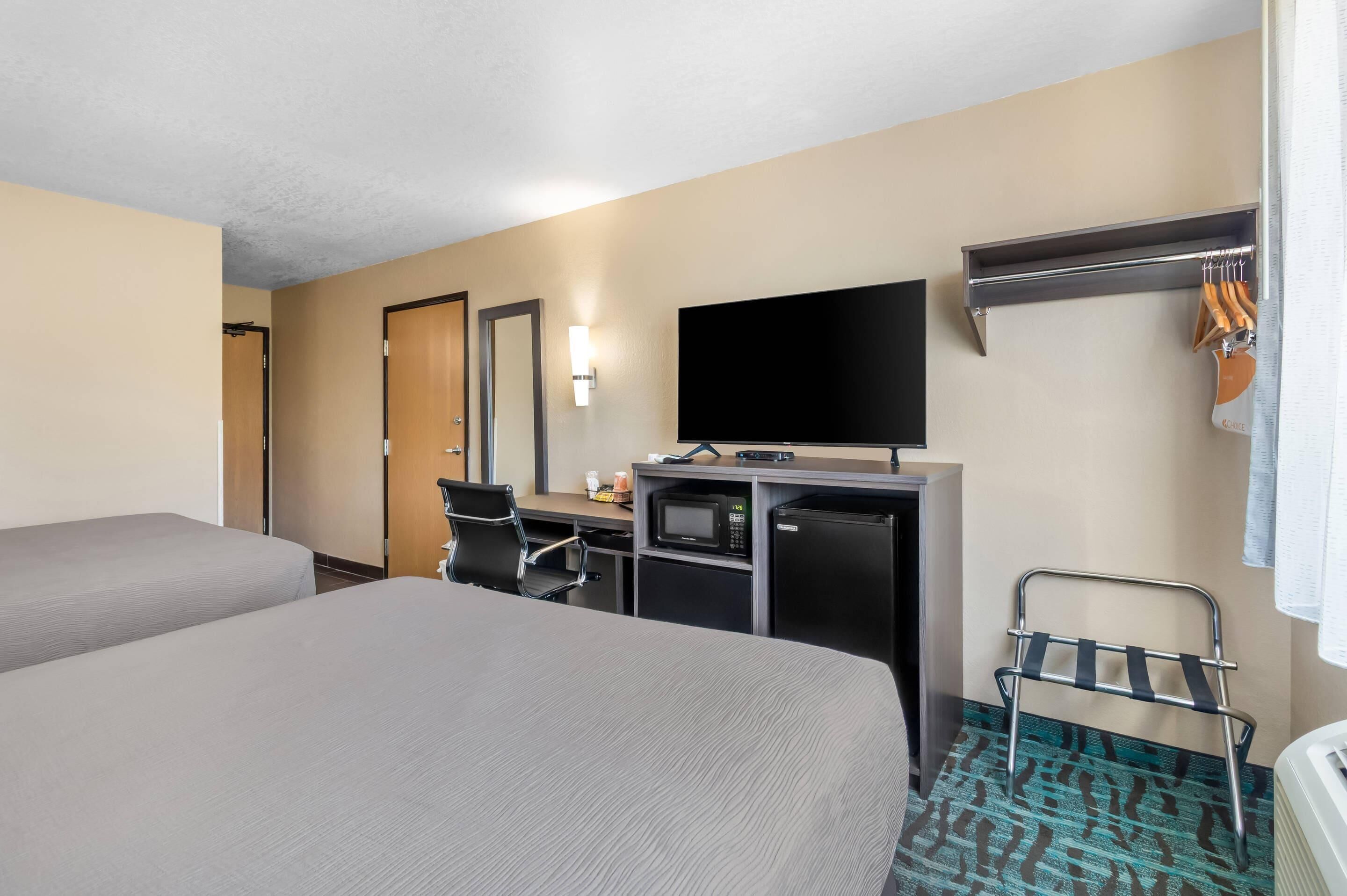 A hotel room with two beds, a desk with a TV, a microwave, and a small fridge.