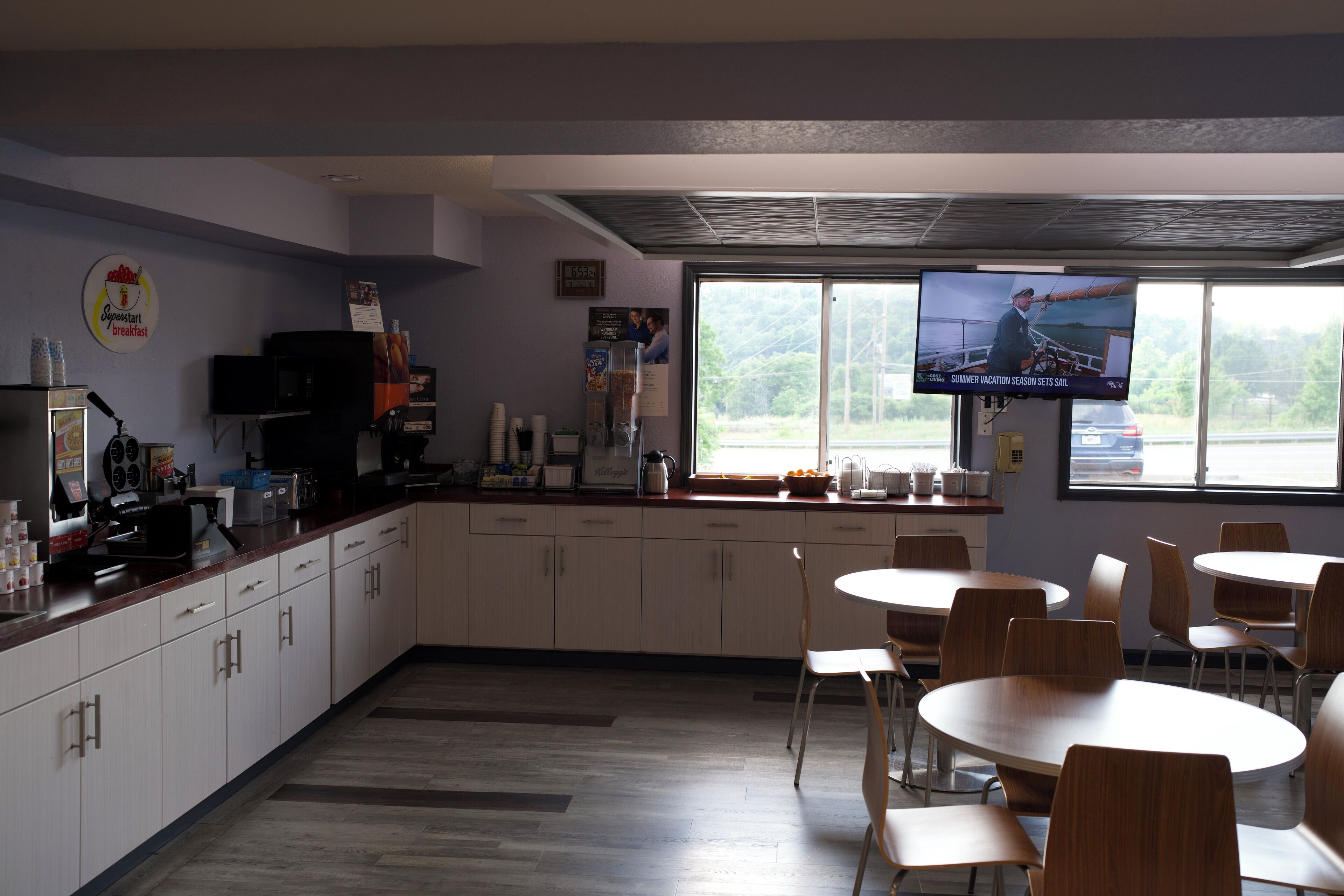 Un restaurante con una televisión mostrando un programa, una zona de cocina y varias mesas y sillas para comer.
