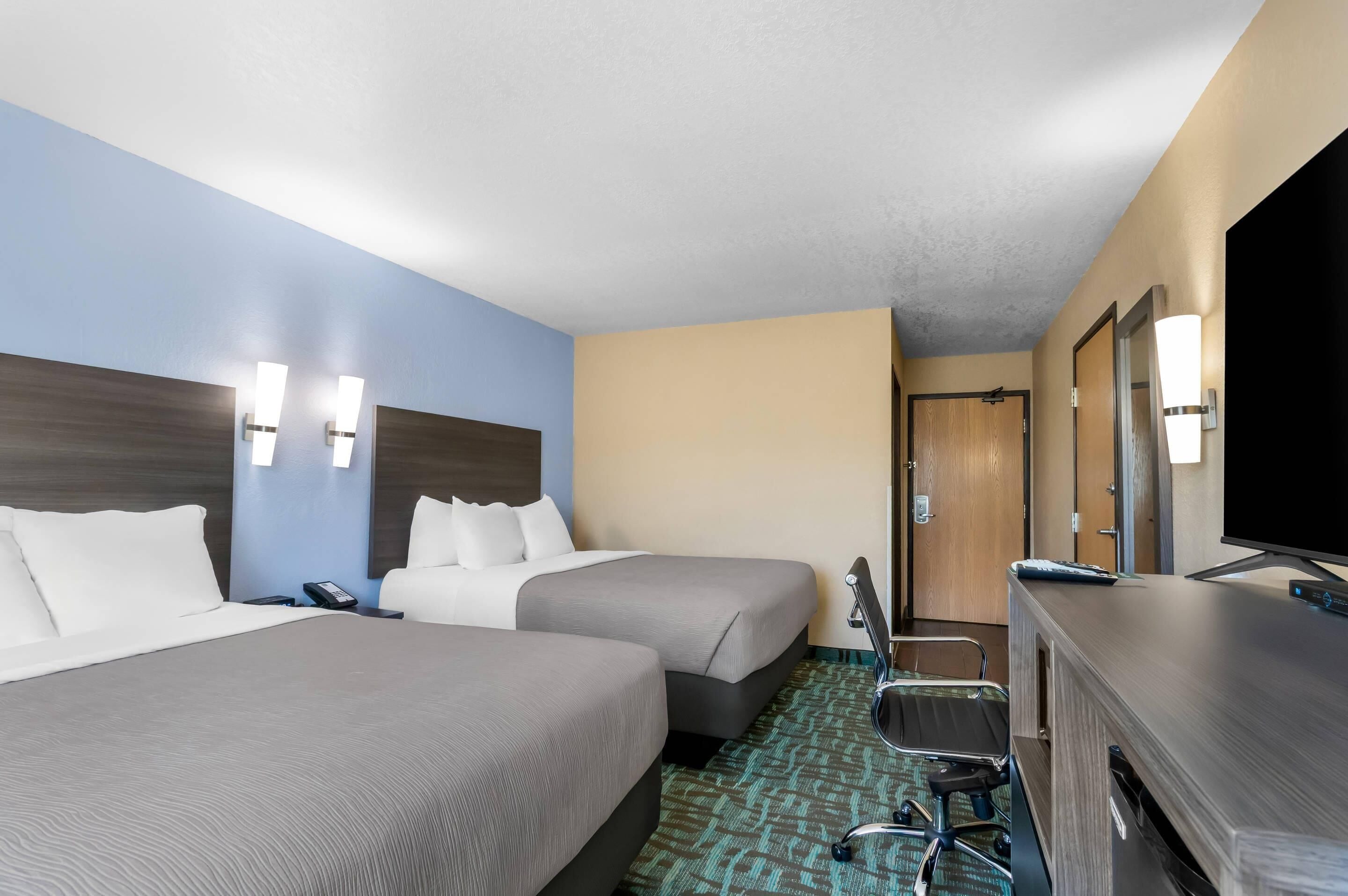 A hotel room with two beds, a desk with a computer, a chair, and a TV.