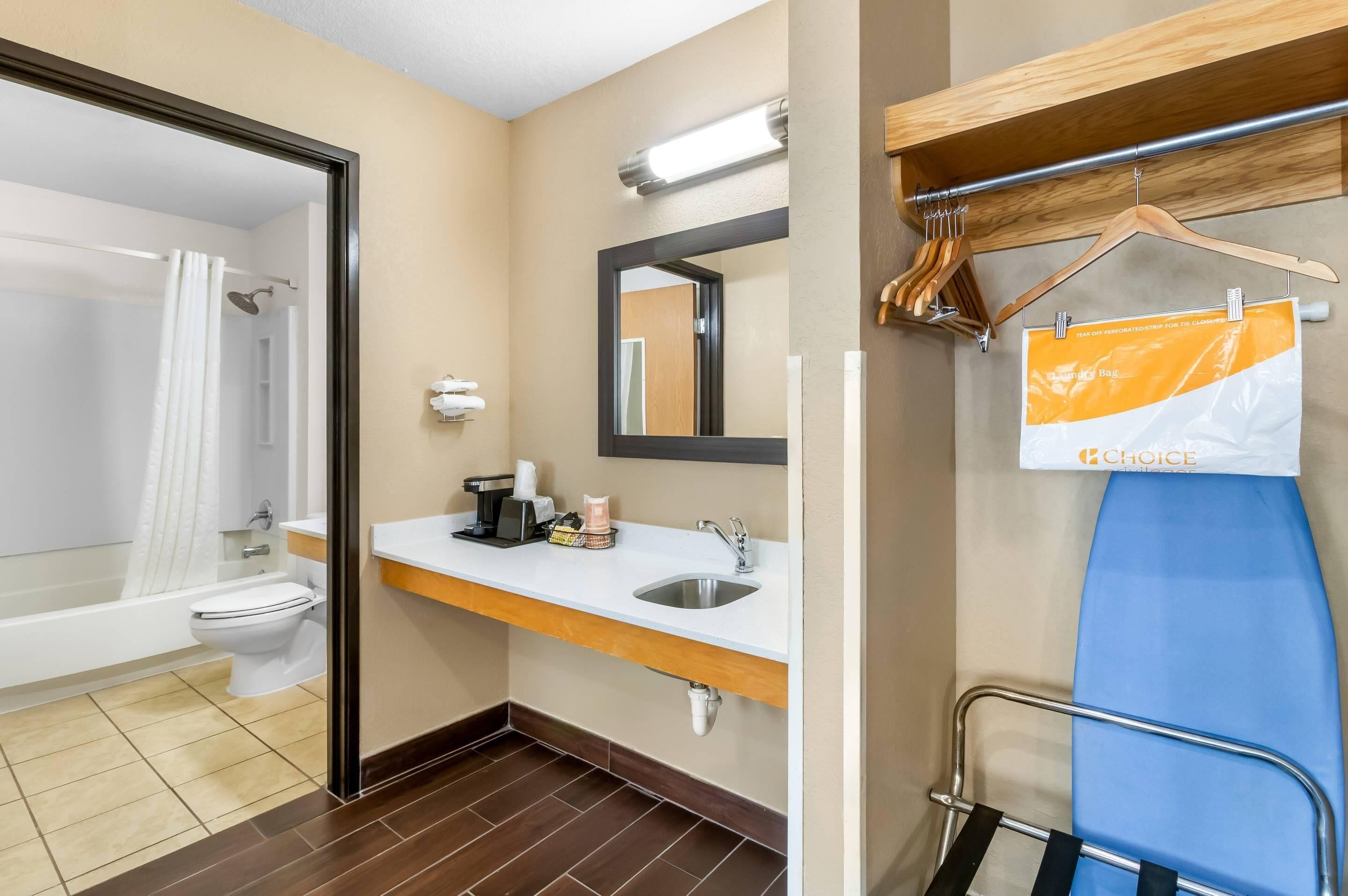 Ein Badezimmer mit Badewanne, Toilette, Waschbecken und Spiegel. Ein Handtuchhalter mit Haken und ein Schild an der Wand sind vorhanden.