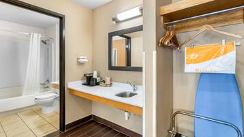 Ein Badezimmer mit Badewanne, Toilette, Waschbecken und Spiegel. Ein Handtuchhalter mit Haken und ein Schild an der Wand sind vorhanden.
