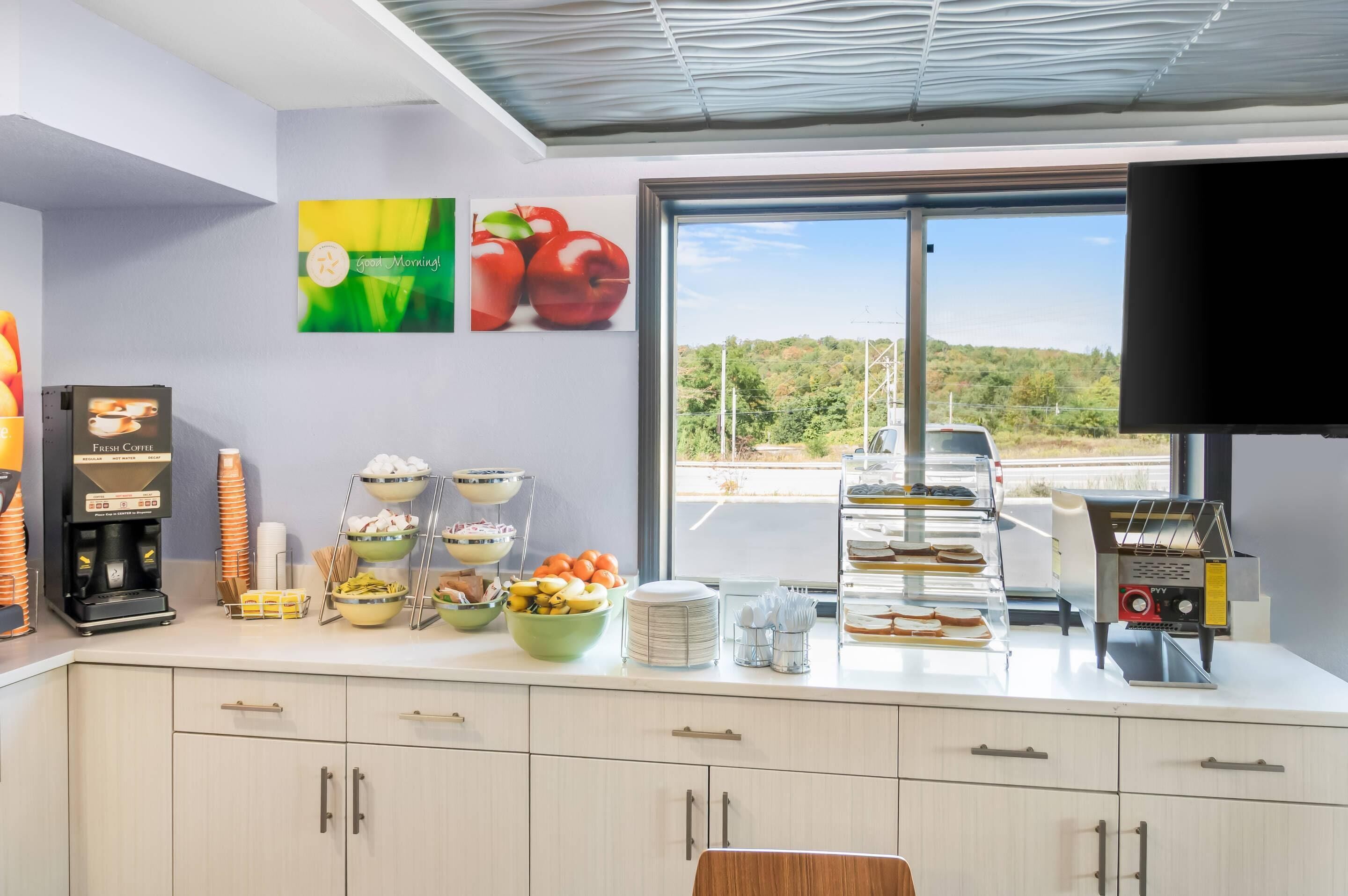 A breakfast bar with coffee machines, fruit bowls, and a view of the road.