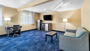 A hotel room with a blue carpet, a desk with a chair, a sofa, a TV mounted on the wall, and a small table.