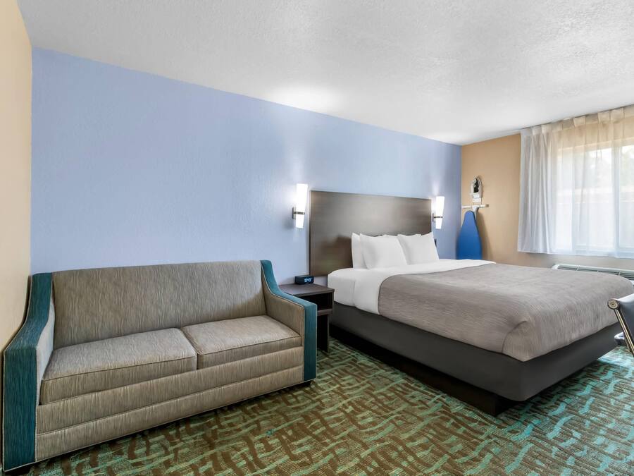 A hotel room with a bed, a sofa, a nightstand, and a window with curtains.