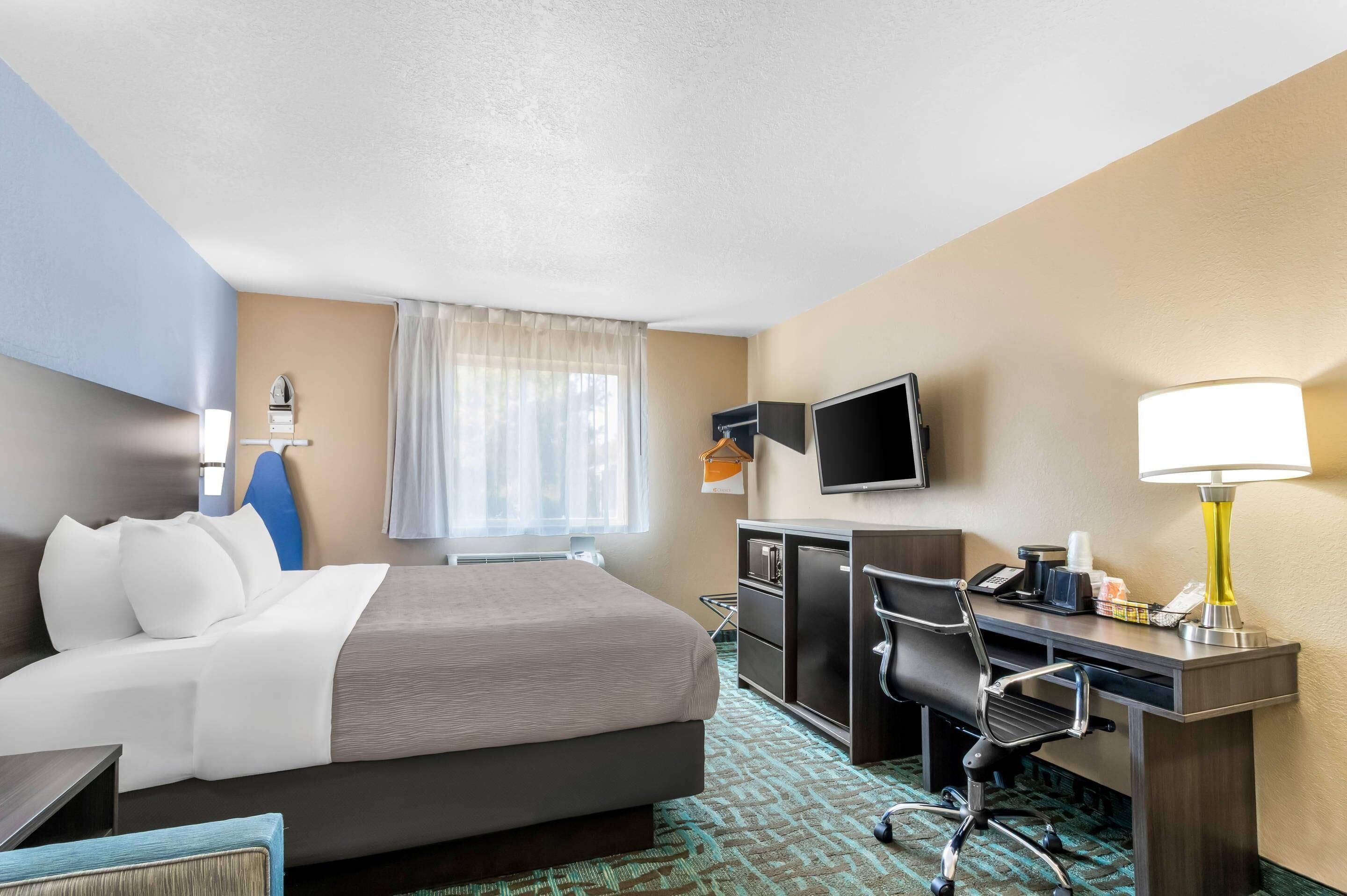 A hotel room with a bed, desk, chair, TV, lamp, and a window with curtains.