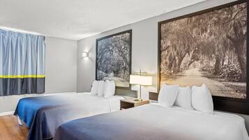 Habitación de hotel con dos camas, una mesita de noche, una lámpara y dos grandes cuadros con motivos forestales en las paredes.