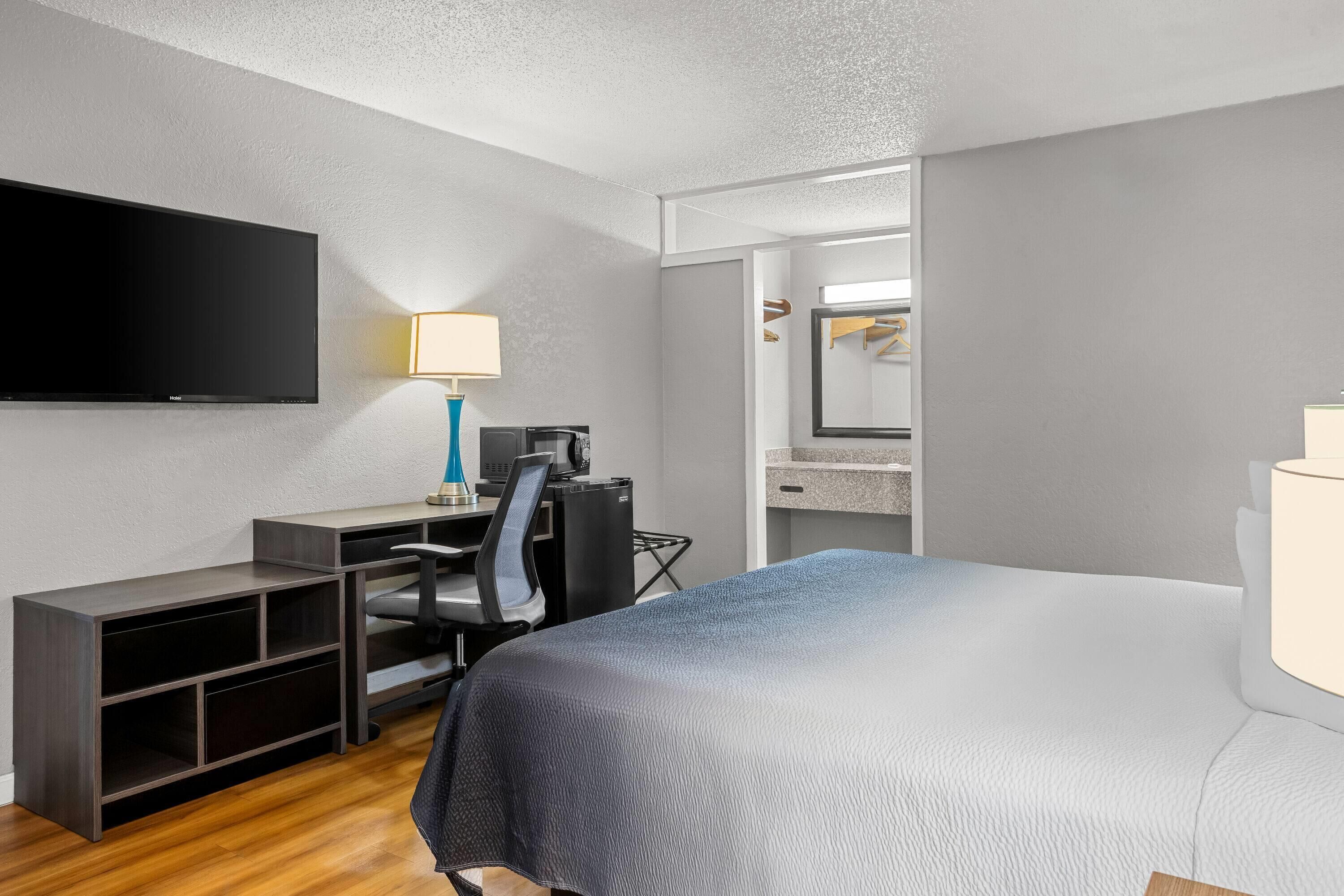 A hotel room with a bed, a desk with a chair, a flat-screen TV, a lamp, a microwave, and a mirror.