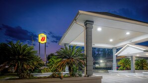 Entree van een Super 8 hotel met overdekte parkeerplaats, palmbomen en een heldere lucht.
