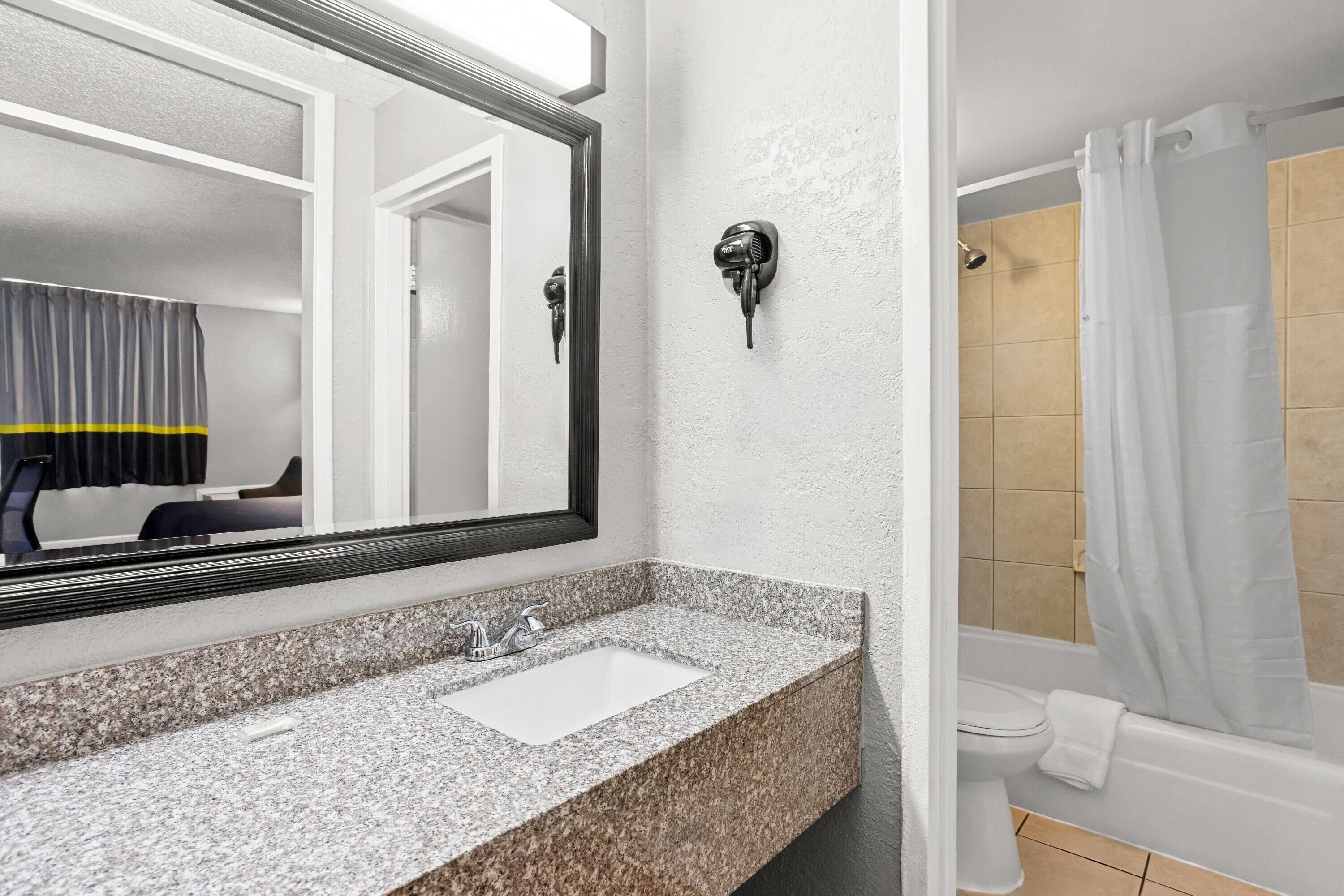 A bathroom with a granite countertop, a sink, a mirror, a shower with a curtain, and a toilet.