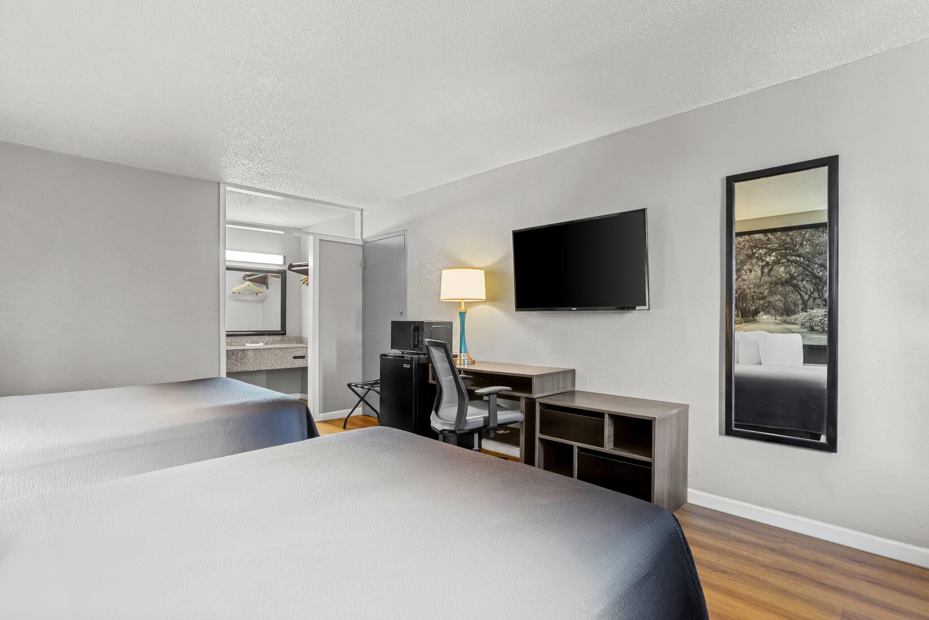 A hotel room with two beds, a desk with a computer, a TV, and a mirror.