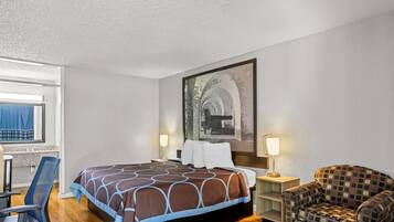 A hotel room with a bed, two bedside lamps, a chair, a desk, and a large framed picture on the wall.