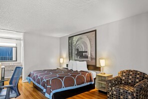 Habitación de hotel con una cama, dos lámparas de noche, una silla, un escritorio y un cuadro grande en la pared.