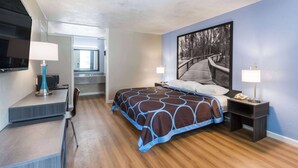 Een moderne hotelkamer met een groot bed, een bureau met een lamp, een stoel, een televisie en een schilderij aan de muur.