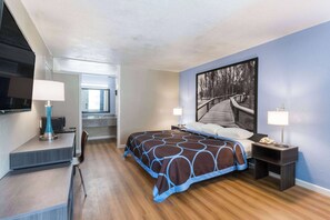 Une chambre d’hôtel moderne avec un grand lit, un bureau avec une lampe, une chaise, un téléviseur et un tableau au mur.