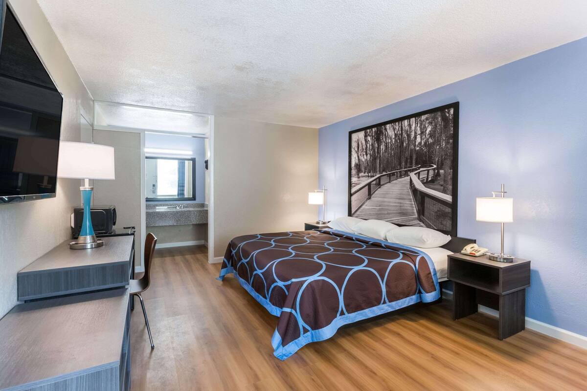 Ein Hotelzimmer mit einem Bett, Nachttischen, einem Schreibtisch, einem Stuhl, einem Fernseher und einem großen Fenster.